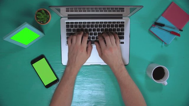 top view man using computer serfing internet or chatting online. on the desk smartphone with green screen photo frame and mug with coffee