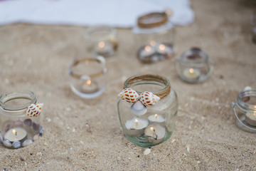 jar with candles and sea shells on the sand 