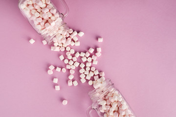 View from above of white and pink marshmallows in two glasses on pink background