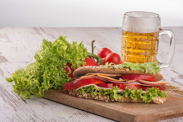 Sandwich with salami, cheese and salad in integral roll with beer mug at wooden background