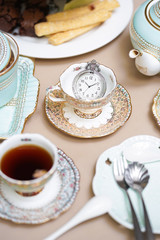 Tea party. Tea time served in the morning with different kind of pastries on the background. Selective focus on the vintage pocket watch.