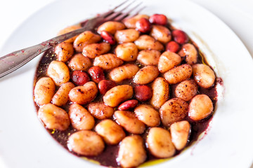 Closeup of fresh vibrant red wine sauce potato gluten free wheat gnocchi on white plate with lupine beans, marinated in Italian Italy restaurant, fork, oil