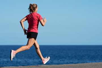 Fitness woman running by the ocean at sunset