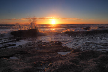 Stunning sunset with orange clouds and spray in the air from the waves crashing onto the limestone...