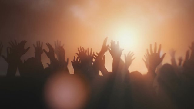 Silhouettes of hands raised in worship with sunlight.