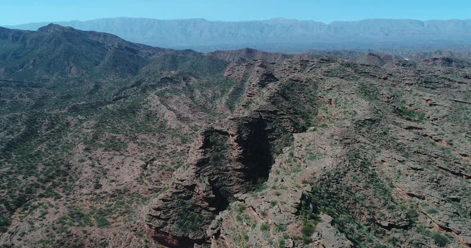 Aerial drone sene of red sandstone cliffs. Flying above ravines and canyons with native vegetation on the top. Famatina mountains at background. Dry rocky landscape at Rioja province, Argentina