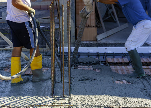 Construction workers pour concrete for the execution of a reinforced concrete floor. The concrete is vibrated after casting