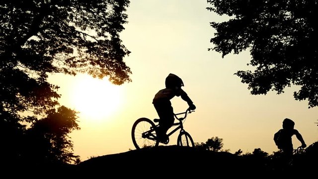 Childrens cycling,Ride up the mound Between two large trees and the sun shines down.Concept Silhouette stay.