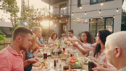 Big Family Garden Party Celebration, Gathered Together at the Table Relatives and Friends, Young and Elderly are Eating, Drinking, Passing Dishes, Joking and Having Fun. - Powered by Adobe