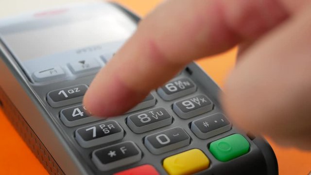 Hand of customer paying with contactless credit card with NFC technology on orange background. Credit card reader machine at bar counter with male holding credit card. Finger entering the PIN code