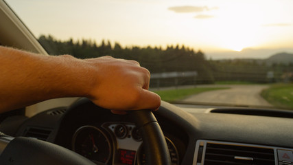CLOSE UP: Unrecognizable man holds the steering wheel while driving at sunset