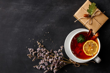 Obraz na płótnie Canvas Autumn composition. A cup of fragrant tea with lemon on a dark table with autumn leaves and flowers.