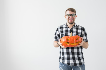 Funny handsome bearded man with carved halloween pumpkin over light background with copy space