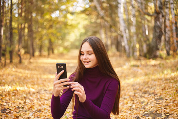 Cute girl with a smartphone in the autumn forest.