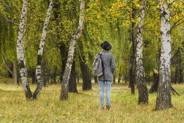Fototapeta premium Girl in a hat with a backpack standing in the autumn forest. Back view