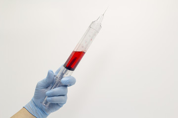 The surgeon's hand in a blue medical glove holds a large syringe with blood . Isolated background.