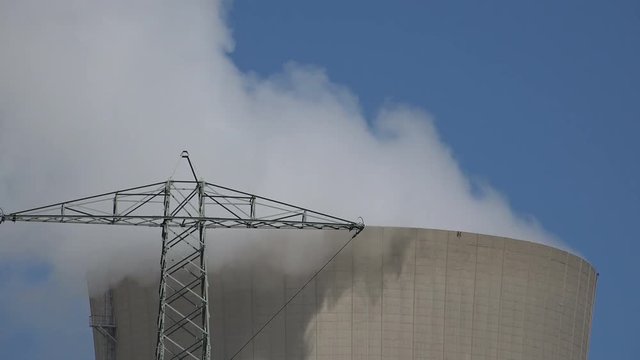 Telephoto shot of the top of a steaming cooling tower. Dark, dramatic clouds and huge amounts of steam suggest pollution.