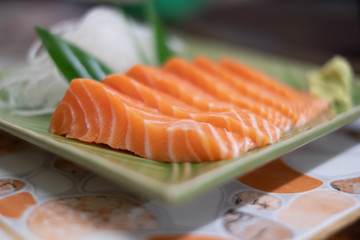Close up of Salmon raw sashimi on green Japanese traditional dish on the table.