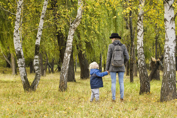 Fototapeta premium Mom and son are walking in the autumn forest. View from the back