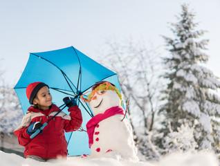 Child with snowman on snow with umbrella