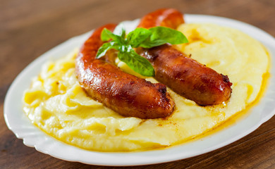fried meat sausages with mashed potatoes in white plate on wooden table background