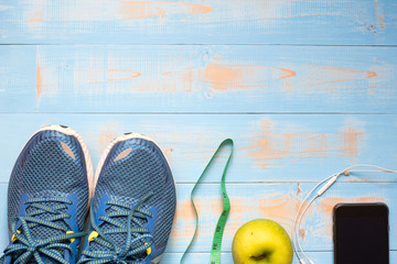 Fitness, Dieting, healthy and lifestyles Concept, Sport Item or exercise accessories, running shoes, apples measuring tape and smartphone with headphone on blue wooden background. copy space for text