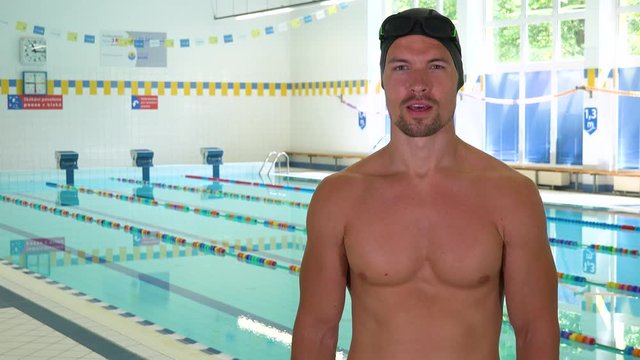 A professional swimmer talks to the camera at an indoor pool