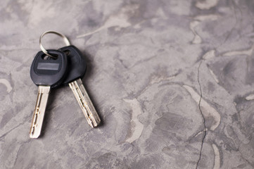 Two shiny metal keys with black plastic handles attached of key ring on gray dirty scratched cement...