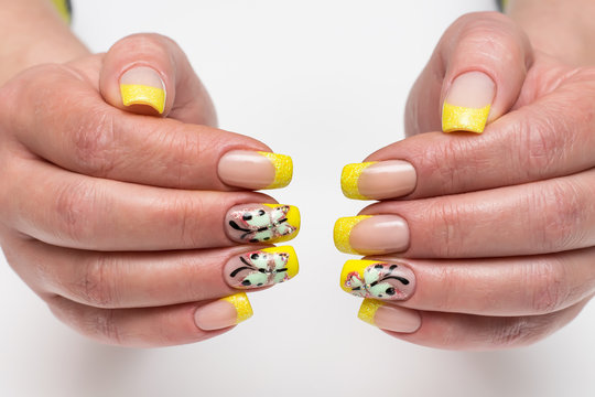 French yellow shiny manicure with painted butterflies and crystals on long, square nails on a white background close-up
