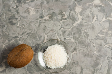 Coconut near heap of coconuts flakes in glass plate on old gray concrete with copy space. Flat lay