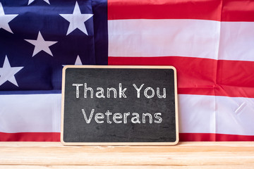 Fototapeta na wymiar Thank You Veterans text written in chalkboard with flag of the United States of America on wooden background. USA holiday of Veterans, Memorial, Independence and Labor Day