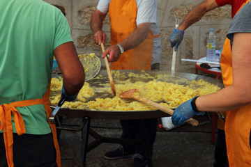 gente removiendo las patatas en una sartén gigante para preparar una tortilla española para una...
