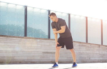 Young and strong guy training outdoor in sportswear. Man in a light of sunset. Sport, health, fitness and urban athletics.