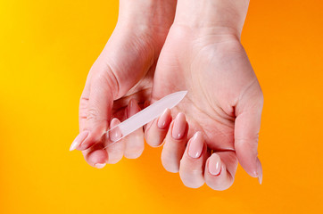 Woman doing a manicure with a glass nail file on an orange background