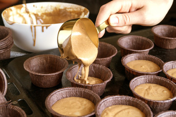 Fototapeta premium Women's hands pour the dough into molds for cupcakes.