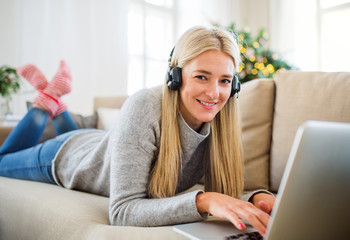 A young woman with headphones and laptop at home at Christmas time.