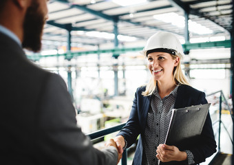 A portrait of an industrial man and woman engineer in a factory, shaking hands.