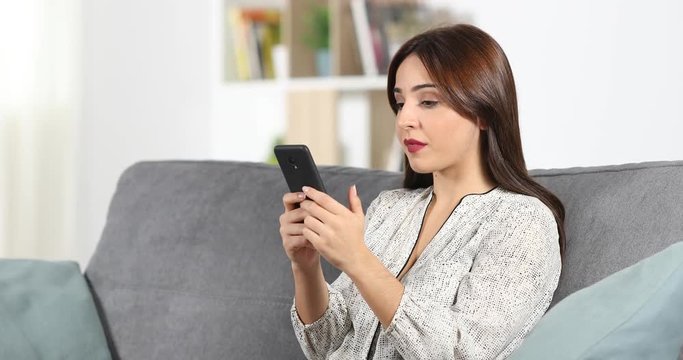 Surprised woman reading good news in a smart phone content sitting on a couch at home