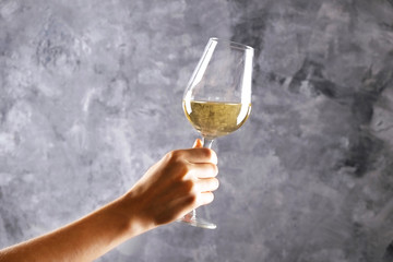 Close up of female arms holding wineglass with expensive hardonnay wine in one hand against light grunged concrete wall background. Cropped shot, copy space for text.