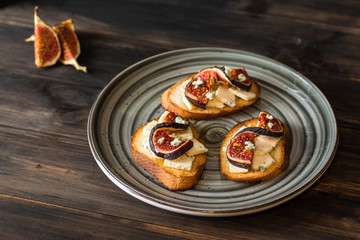 Sandwiches with ricotta, fresh figs, walnuts and honey on rustic wooden board over black backdrop, top view. Bruschetta with figs. Aperitive. Mediterranean cuisine. Crostini.