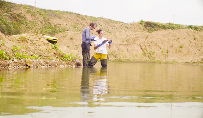 Fototapeta na wymiar Two environmental scientists standing in the water. A woman checking with the GPS navigator and marking point of research on the map.