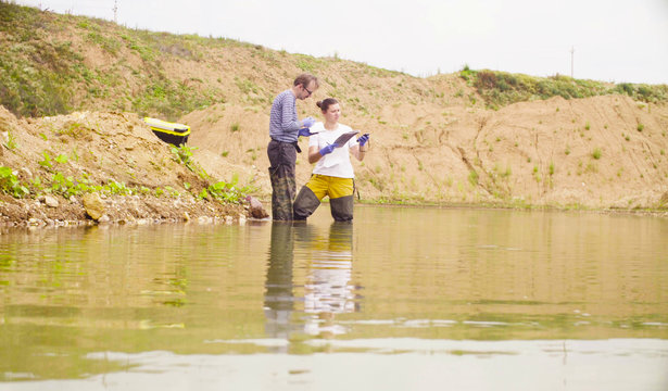 Two environmental scientists standing in the water. A woman checking with the GPS navigator and marking point of research on the map.