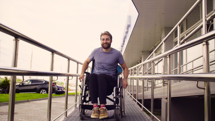 Young disabled man in a wheelchair riding down the slope and smiling