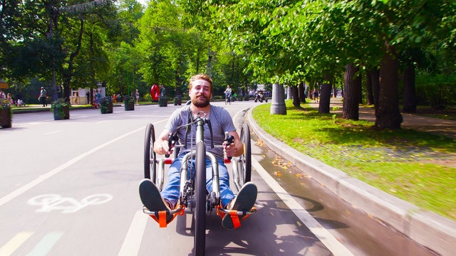 Face view of happy young disable man riding hand bike in the park. He smiling. - Powered by Adobe