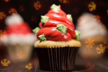there are a lot of cupcakes on the board, in the foreground a cupcake with cream in the shape of a Christmas tree, surrounded by bokeh of snowflakes, holiday concept