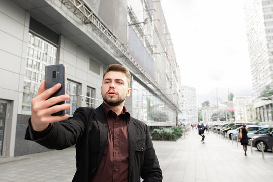 Portrait of a business man with a beard and dressed in a suit, walking around the streets of the city and takes selfie. Man speaks on video communication on the street.