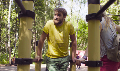 Young disable man in the park with his wife. The man is doing exercises on the parallel bars.