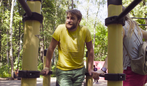 Young disable man in the park with his wife. The man is doing exercises on the parallel bars.
