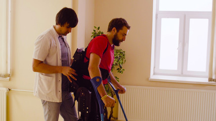 Young disable man in the robotic exoskeleton sitting in wheelchair in the rehabilitation clinic