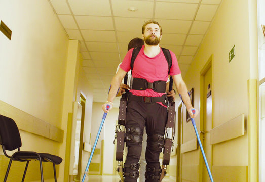 Young disable man in the robotic exoskeleton sitting in wheelchair in the rehabilitation clinic